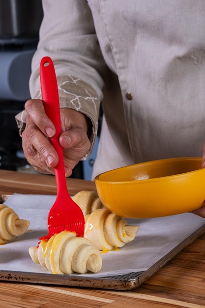 Die Hand der Frau bürstet geschlagenes Ei auf Croissants, um sie in den Ofen zu stecken