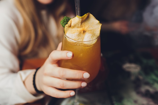 Die Hand der Frau, die altmodisches Glas mit kaltem Cocktail gegen unscharfen Nachtclubhintergrund hält.