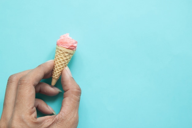 Die Hand der Frau, die gebissene Pastellmeringe auf Eistüte mit blauem Hintergrund hält