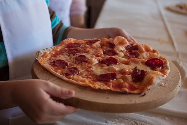 Die Hand der Frau, die Pizza auf einem mit Mehl bestreuten Holzschneidebrett hält