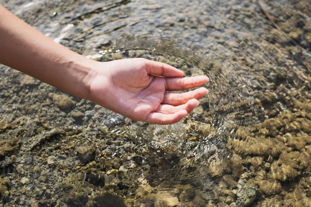 Die Hand der Frau, die Wasser mitten in der Natur berührt