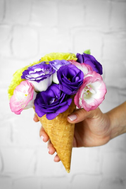 Die Hand der Frau, die wilde Blumen im Wafer auf hellem Wandhintergrund hält