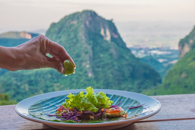 Die Hand der Frau drückt die Zitrone in einen Salat mit der schönen Landschaft