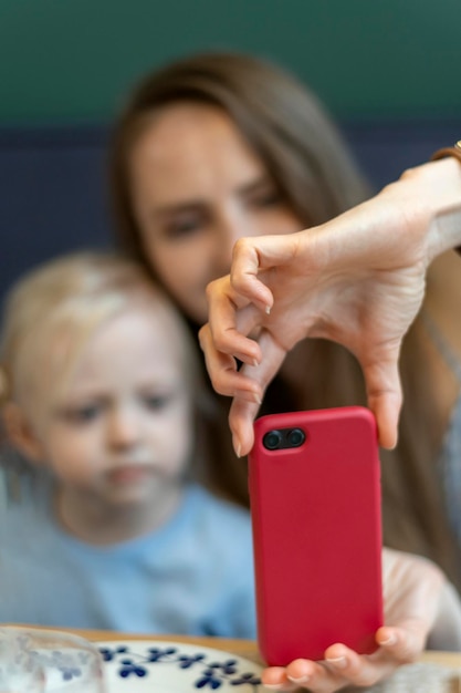 Die Hand der Frau hält das Telefon vor dem verschwommenen Hintergrund von Mutter und Tochter Frau mit Kind macht Selfie auf dem Smartphone