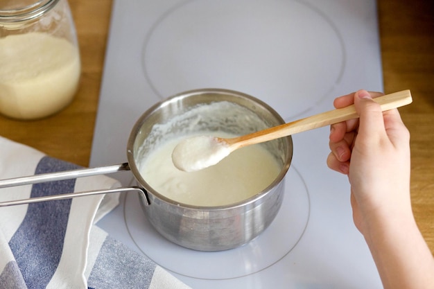 Die Hand der Frau hält einen Holzlöffel Haferbrei über einem Topf Kochen von Grieß auf einem weißen Elektroherd