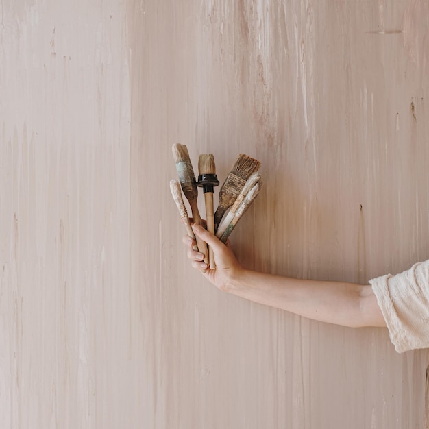 Die Hand der Frau hält Pinsel auf neutralem beigem Hintergrund Minimalistisches Kunstkonzept