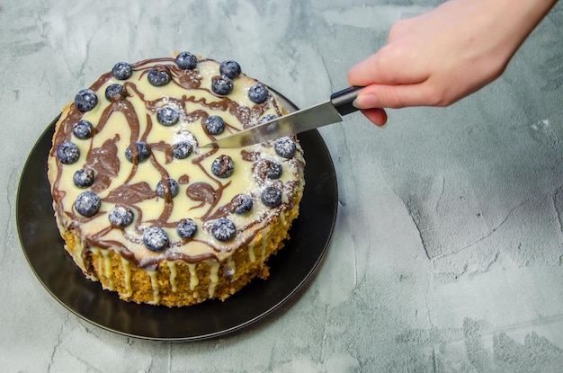 Die Hand der Frau schneidet großen hausgemachten Kuchen mit Messer auf dem Hintergrund einer Betontischplatte