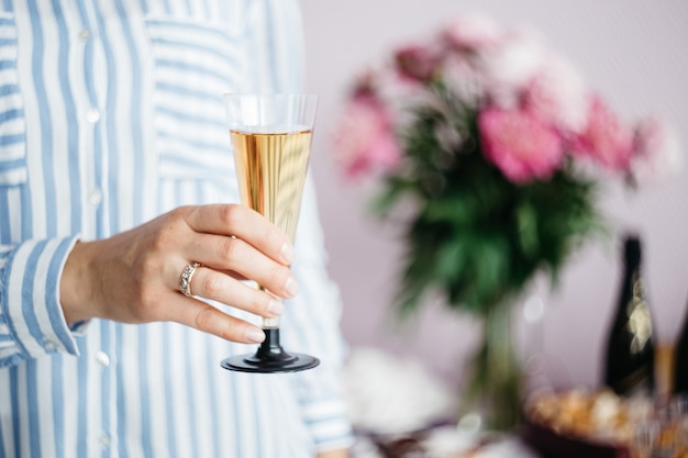Die Hand der Frauen, die ein Glas Champagner auf dem Hintergrund der festlichen Tabelle hält