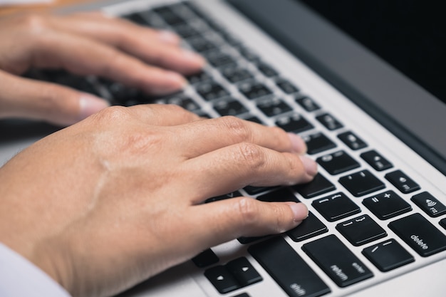 Die Hand der Geschäftsfrau, die auf Laptoptastatur am Büroarbeitsplatz schreibt