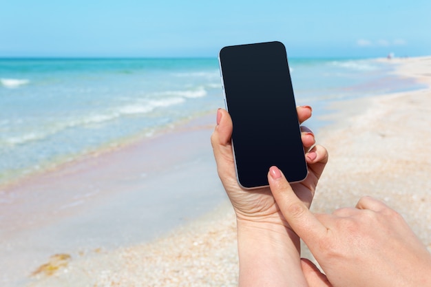 Die Hand der Schönheit unter Verwendung des intelligenten Telefons am Strand