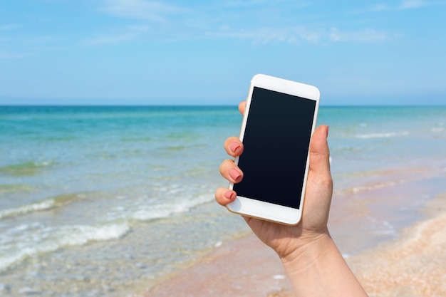 Die Hand der Schönheit unter Verwendung des intelligenten Telefons am Strand