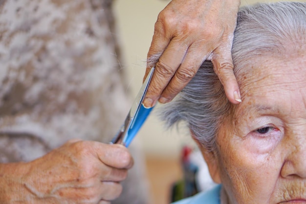 Die Hand des Friseurs schneidet eine ältere alte Dame mit einer Haarschneideschere oder einem Haarschneidekamm