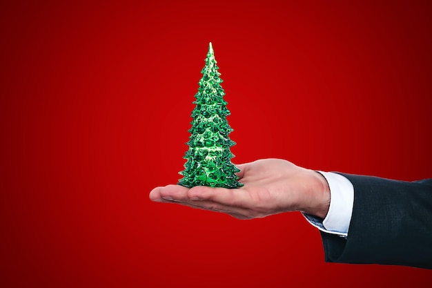 Die Hand des Geschäftsmannes im Anzug hält einen kleinen grünen Weihnachtsbaum auf seiner Handfläche Spezielles Geschäftsangebot des Konzepts