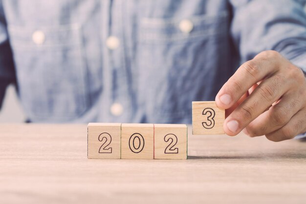 Die Hand des Geschäftsmannes sortiert einen Holzwürfel mit der Zahl 2023 auf dem Tisch aus Arbeitskonzept in