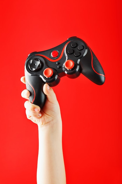 Die Hand des Kindes hält triumphierend das Gamepad auf einer roten Oberfläche