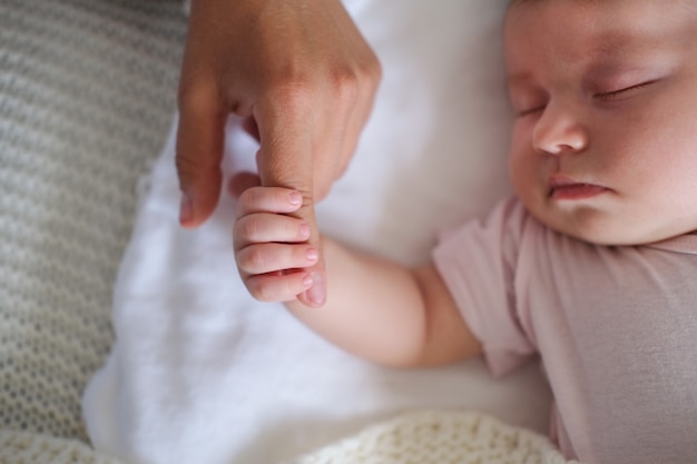 Die Hand des kleinen Babys hält den Finger der Mutter. Glückliche Familie. Genießen Sie die gemeinsame Zeit zu Hause. Zeitlupe. Liebe. Süss. Zärtlichkeit.