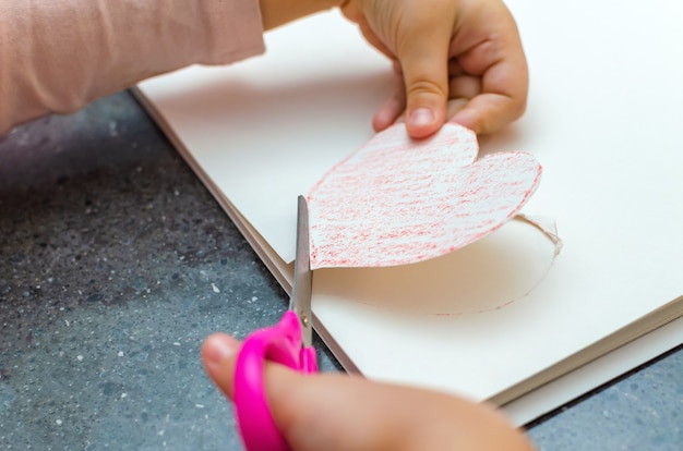 Die Hand des Mädchens hält ein aus Papier geschnittenes Herz. Kreativität der Kinder - Zeichnen und Basteln zum Valentinstag oder Muttertag.