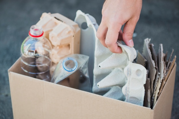 Die Hand des Mannes, die Plastikflaschen und Eierkarton im Recyclingkasten sammelt