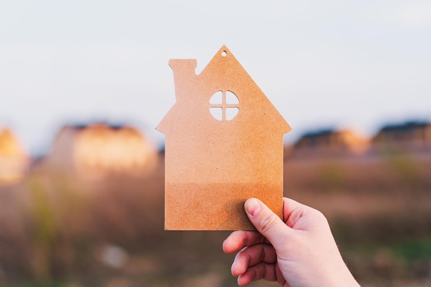 Die Hand des Mannes hält ein Holzhaus auf dem Hintergrund von verschwommenen Gebäuden