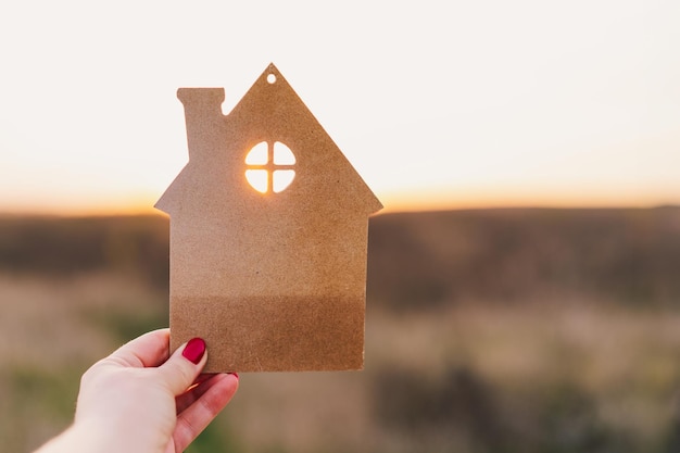 Die Hand des Mannes hält ein Holzhaus auf dem Hintergrund von verschwommenen Gebäuden