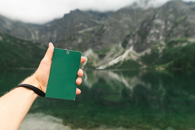 Die Hand des Mannes hält einen leeren grünen Turgid vor dem Hintergrund des Lake Morskie Oko. Speicherplatz kopieren. Freiraum