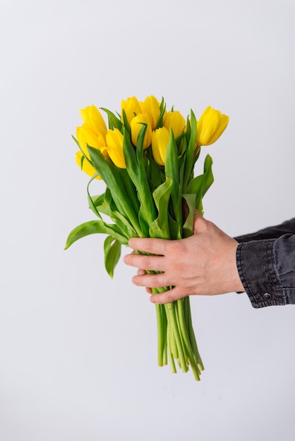 Die Hand des Mannes hält einen Strauß gelber Tulpen. Liebessymbol