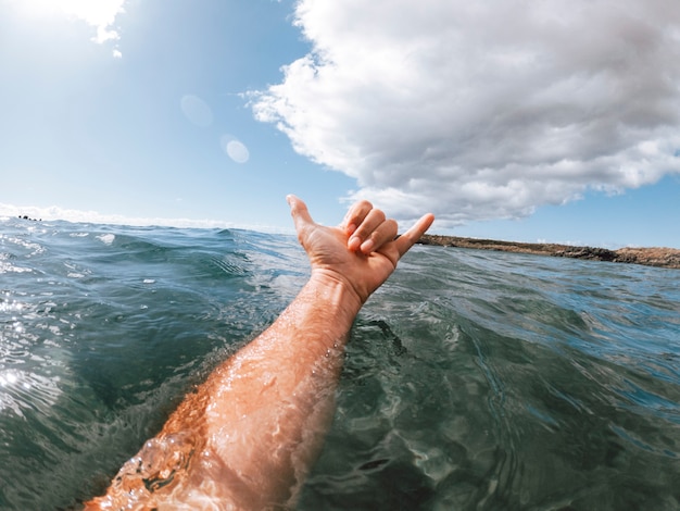 Die Hand des Mannes im Brandungszeichen aus dem blauen Ozeanwasser