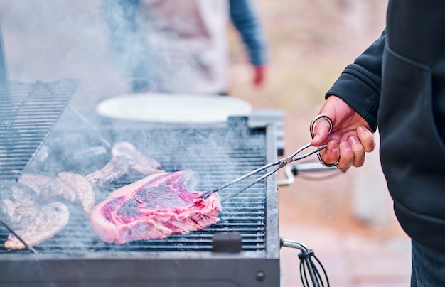 Die hand des mannes kocht ein großes rindersteak auf dem grill.