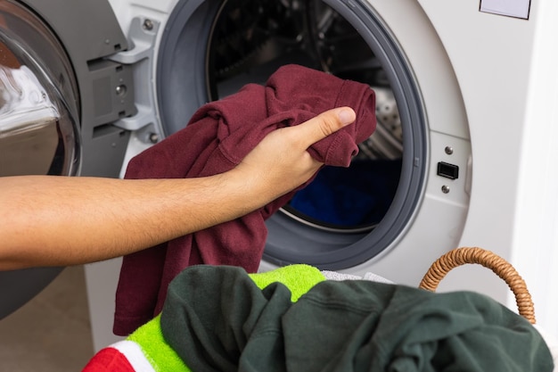 Die Hand des Mannes öffnet die Vorderseite der Waschmaschine und ist dabei, die schmutzige Wäsche in die Wäsche zu geben