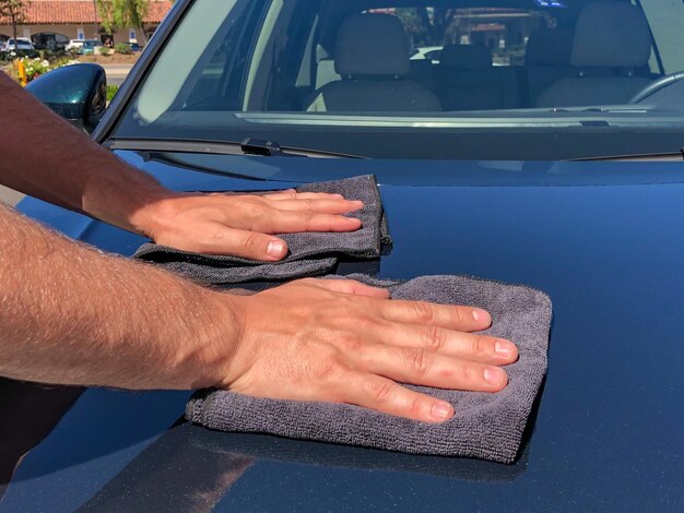 Die Hand des Mannes reinigt das Auto mit einem schwarzen Mikrofasertuch. Wischen Sie die Oberfläche des Autos mit der Hand ab.