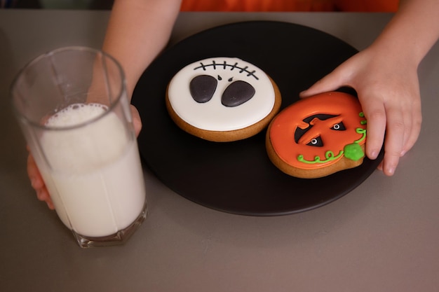 Die Hand des Nahaufnahmemädchens nimmt Lebkuchenkürbis vom Tischhalloween-Feiertag