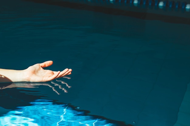 Die Hand des Schwimmers taucht in ein Wasserbecken mit blauem, transparentem, klarem Wasser ein, auf das helles Sonnenlicht scheint