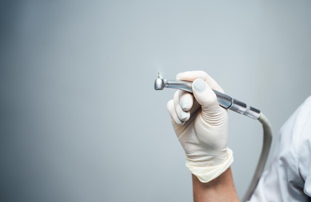 Die Hand des Zahnarztes in weißem Handschuh hält das Instrument Bormaschine Instrument des Zahnarztes auf dem Hintergrund der Lichtklinik Nahaufnahme