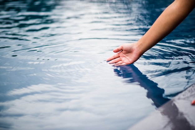 Die Hand, die das blaue Wasser berührt.