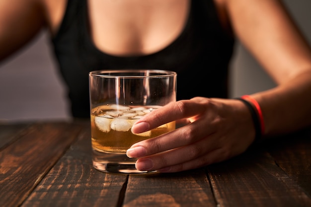 Die Hand einer betrunkenen Frau, die ein Glas Alkohol hält. Konzept von Alkoholismus und Sucht.