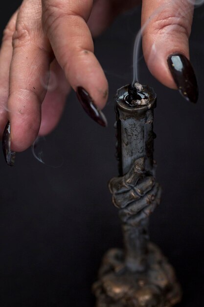 Die Hand einer erwachsenen weiblichen Hexe löscht eine Kerze mit ihren Fingern in der dunklen Okkultismus-Magie und Zauberei Vertikal