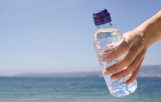 Die Hand einer Frau, die eine Flasche kaltes Wasser am Strand hält