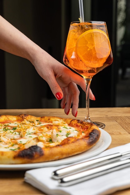 Die Hand einer Frau greift nach einer Pizza und einem Glas orangefarbener Flüssigkeit.