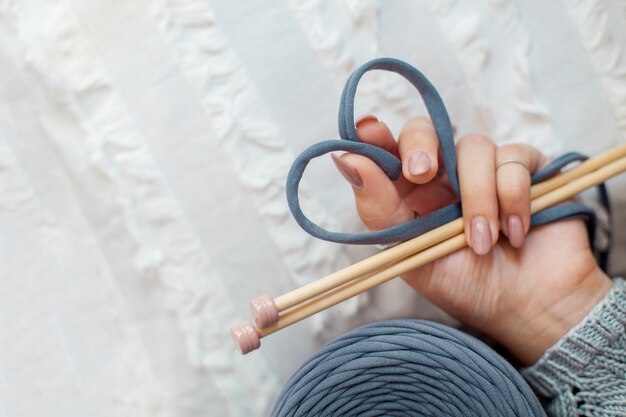 Die Hand einer Frau hält ein blaues Strickgarn und faltet es in Form eines Herzens. Konzept der Liebe zum Stricken und Basteln.