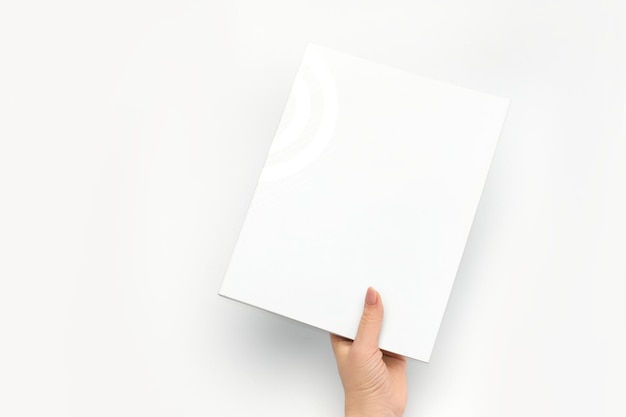 Die Hand einer Frau hält ein geschlossenes Buch mit einem leeren weißen Einband auf einem weißen Hintergrund