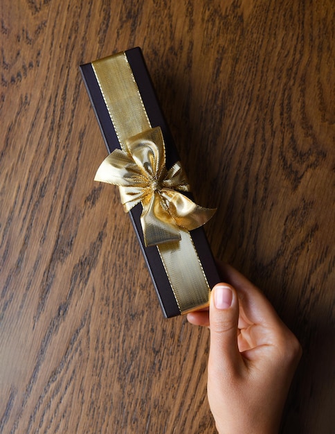 Die Hand einer Frau hält eine braune Geschenkbox mit einer goldenen Schleife