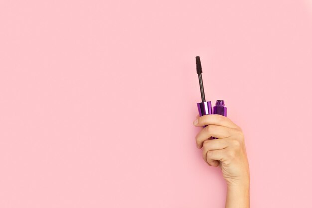 Foto die hand einer frau hält eine mascara-flasche auf einem rosa hintergrund.