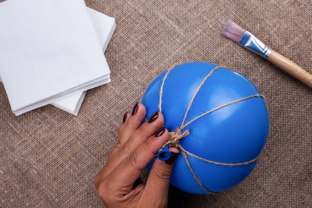 Die Hand einer Frau hält einen Ballon in Juteseil gewickelt, der Prozess der Herstellung eines Pappmaché-Kürbises, Halloween-Dekor.