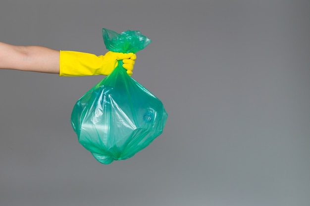 Die Hand einer Frau in einem Gummihandschuh hält einen transparenten grünen Müllsack