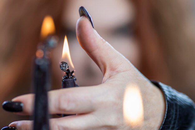 Die Hand einer Frau mit einer schwarzen Maniküre hält eine brennende Kerze. Mystik und okkulte Nahaufnahme. Selektiver Fokus