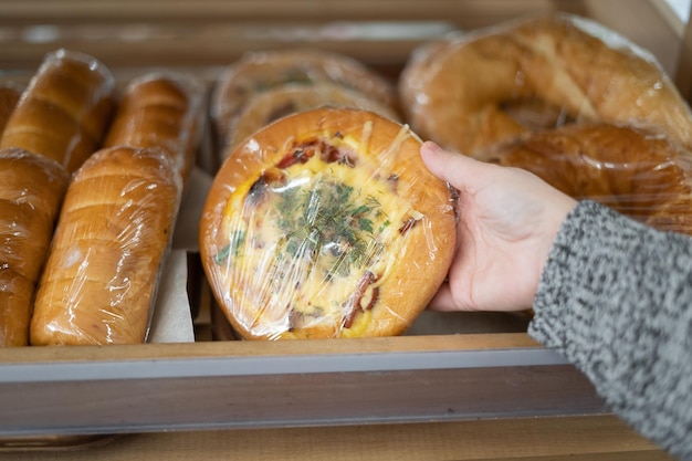 Die Hand einer Frau nimmt eine kleine weiße Mehlpizza aus einem Holzregal in einem Supermarkt in der Nähe Backverkauf Kopierraum