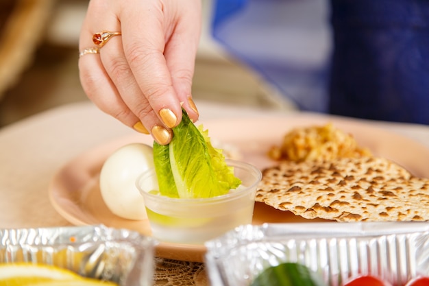 Die Hand einer Frau taucht während des Pesach Seder ein Salatblatt in Salzwasser. Horizontales Foto