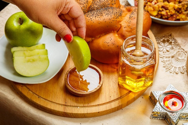 Die Hand einer Frau taucht zu Ehren der Feier von Rosh Hashanah am Tisch ein Stück Apfel in Honig