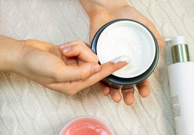 Die Hand einer jungen Frau nimmt eine Gesichtscreme aus dem Glas. Hautpflege, Feuchtigkeit und Ernährung.