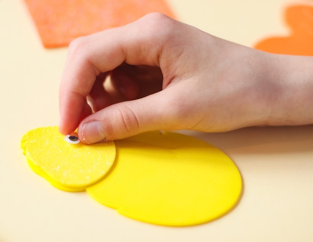 Die Hand einer kaukasischen Teenagerin klebt ein dekoratives Auge auf ein gelbes Küken aus Filz